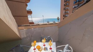 Un balcon avec une table préparée pour prendre un verre, donnant sur une plage et l’océan.