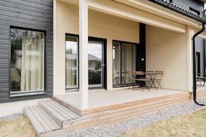 A modern house with a covered porch, a wooden deck, and a table with chairs.