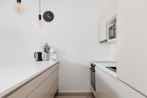 A modern kitchen with a white countertop, a black clock, a coffee maker, and a kettle.