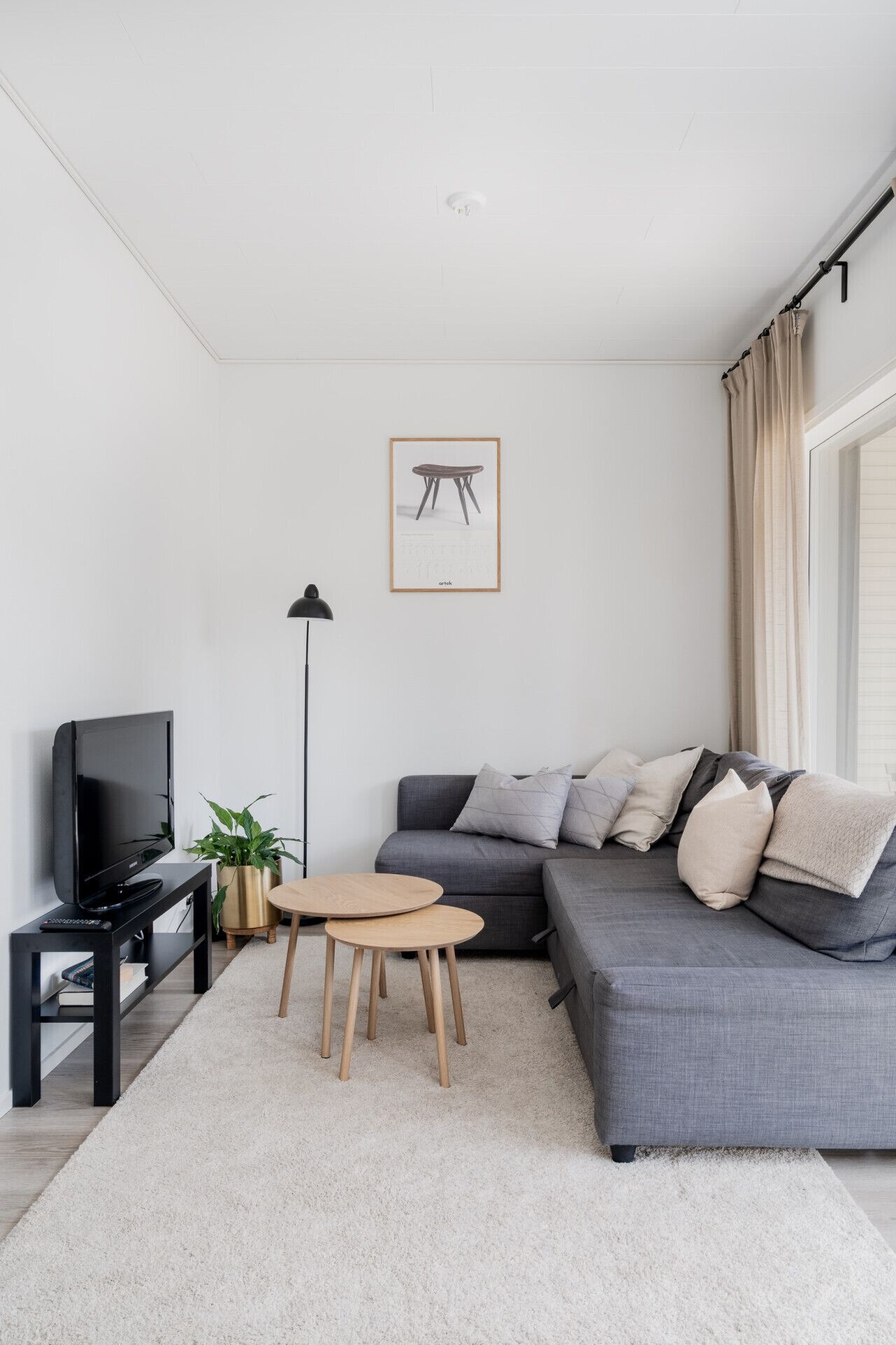 A modern living room with a grey sofa, a small round table, a black TV stand, and a floor lamp.