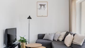 A modern living room with a grey sofa, a small round table, a black TV stand, and a floor lamp.