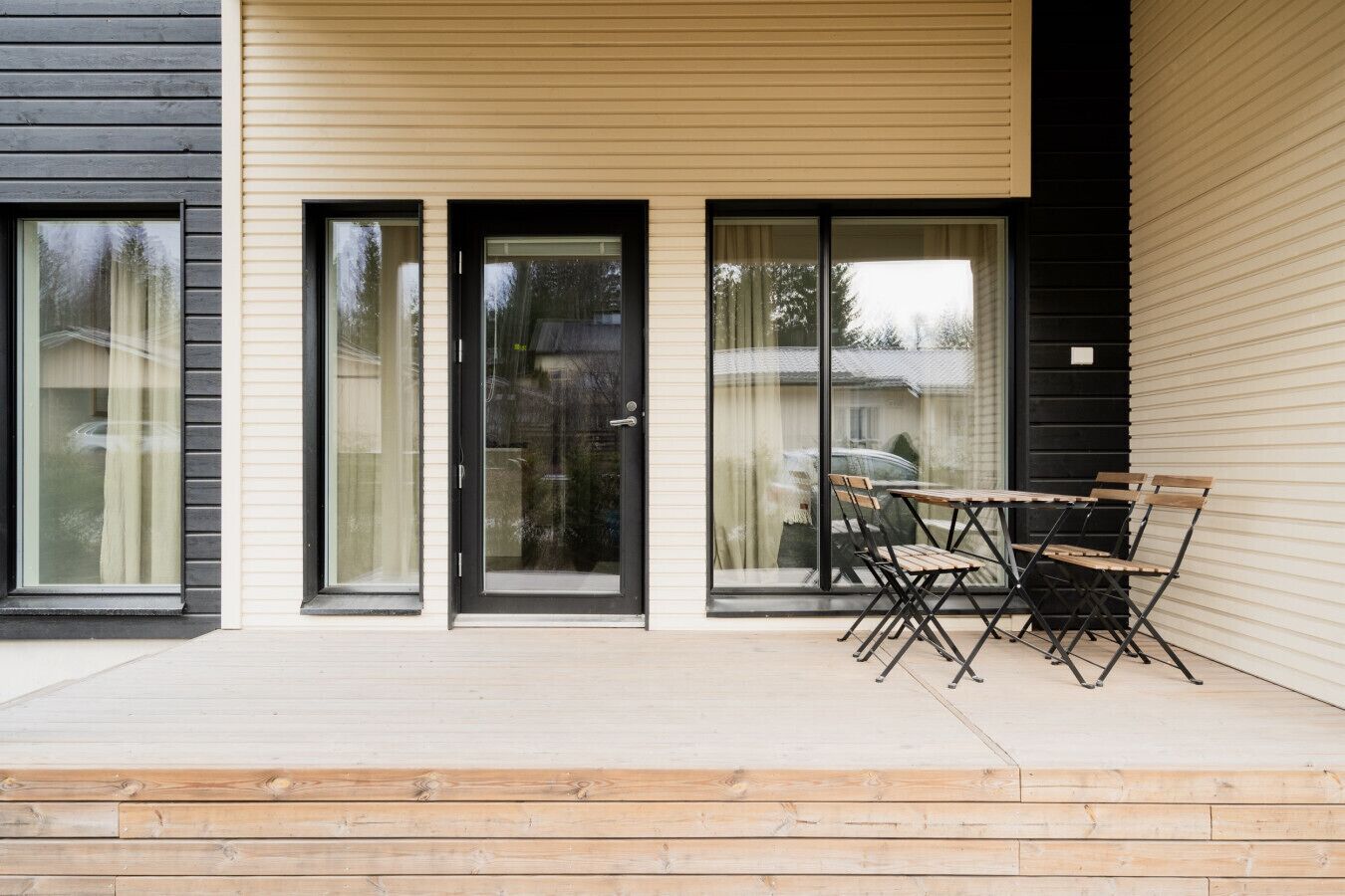 A modern building with large sliding glass doors, a wooden deck, and a table with chairs.