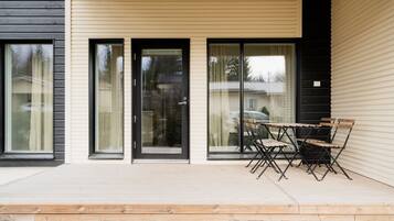 A modern building with large sliding glass doors, a wooden deck, and a table with chairs.