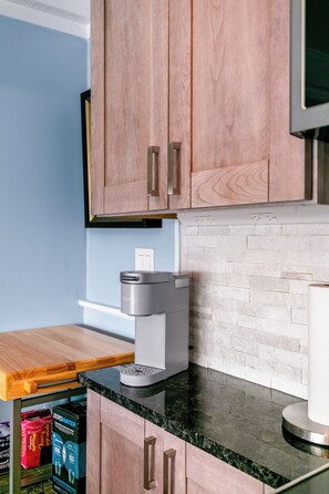 A kitchen with wooden cabinets, a countertop, a coffee maker, and a box of bottled water. - Perfect Ptown Stay, Dogs Welcome, Walk Everywhere (Provincetown)