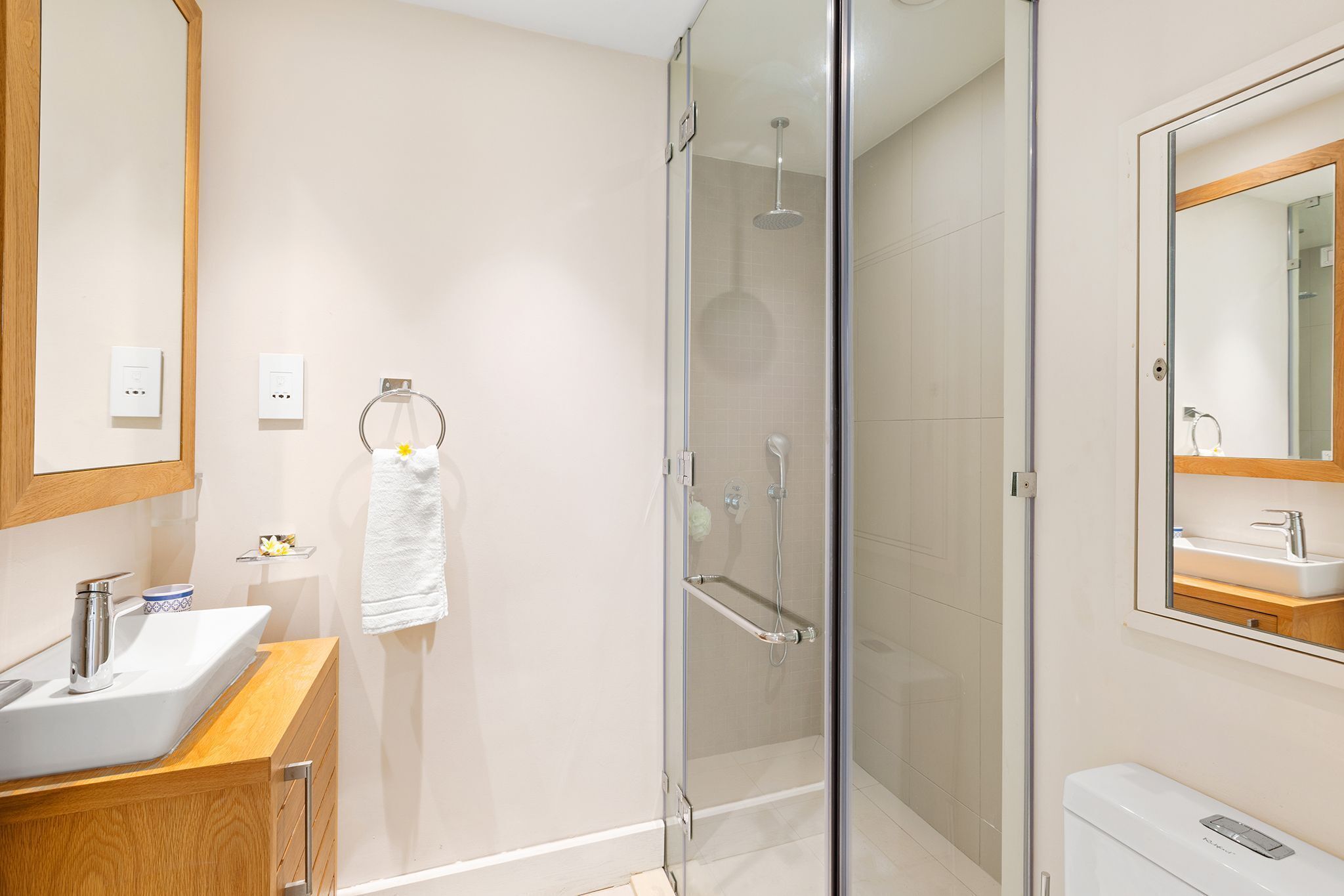 A modern bathroom with a glass-enclosed shower, a wooden vanity with a sink, and a large mirror above the sink.