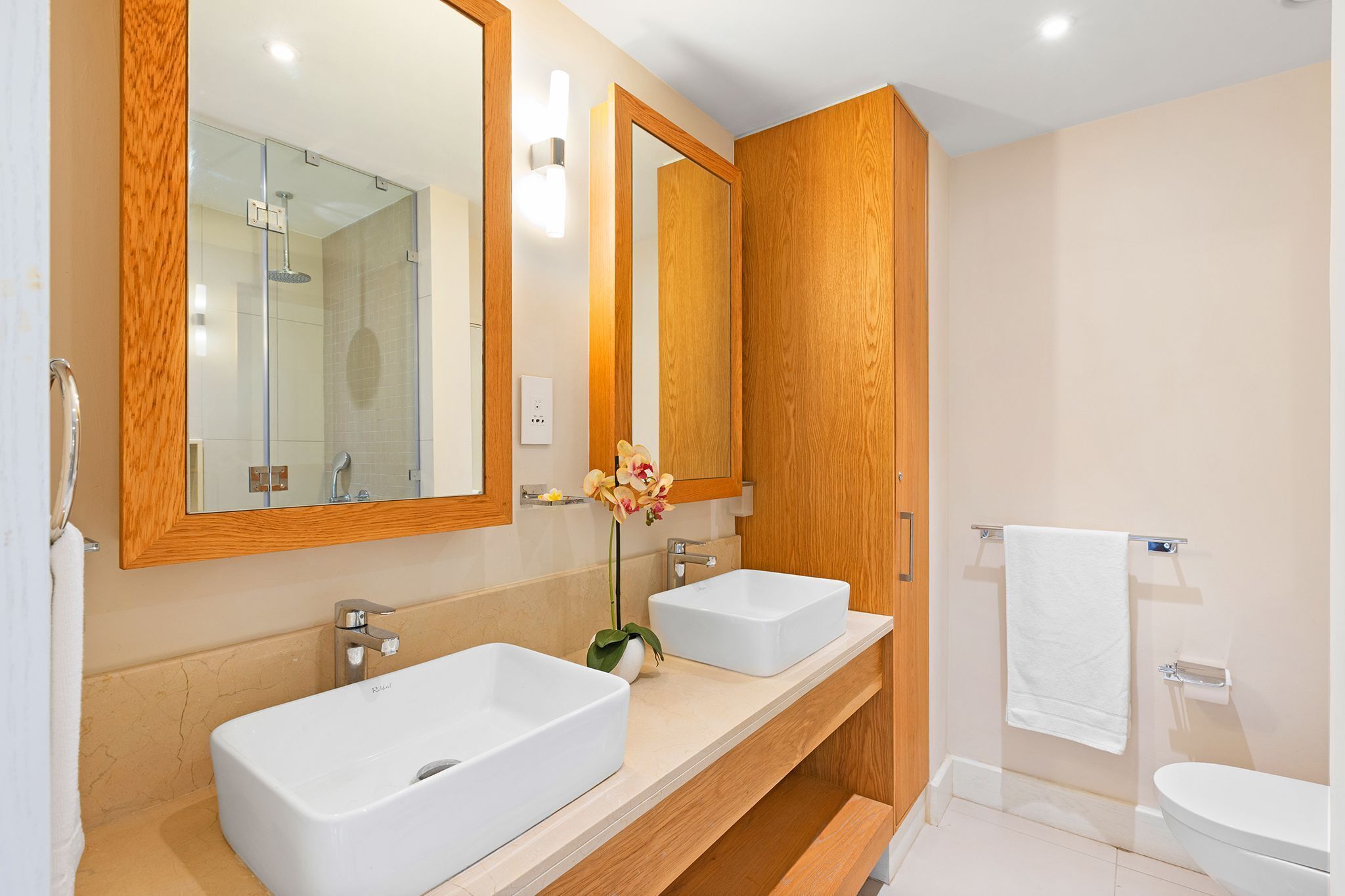 A modern bathroom with two sinks, a shower, and a toilet.