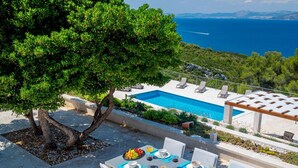 A dining area with a table set for four, overlooking a pool and the sea. - Stay With Panoramic Sea Views (Pucisca)