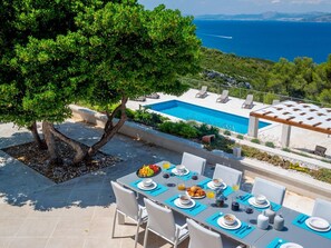 Ein Essbereich mit Tisch für vier Personen, mit Blick auf einen Pool und das Meer.
