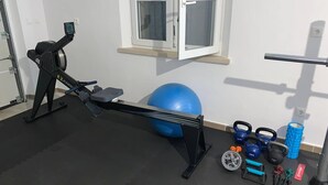 A home gym with a rowing machine, exercise ball, kettlebells, and resistance bands. - Stay With Panoramic Sea Views (Pucisca)