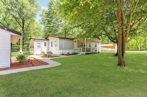 A single-story mobile home with a covered porch, a small front yard with a red mulch garden, and a large tree to the right. - Outdoor Sports & Rec Hideaway w/Hiking & Hot Tub! (Pullman)