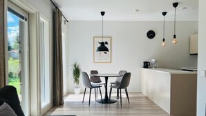 A modern living room with a sofa, a dining table with chairs, a kitchen area, and a large window with curtains. - Modern 3BR House with Sauna & Parking (Vantaa)