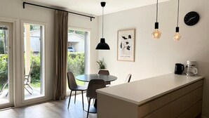 A modern kitchen with a central island, pendant lights, a clock, and a framed botanical print on the wall. - Modern 3BR House with Sauna & Parking (Vantaa)