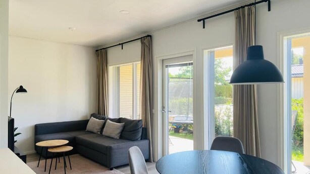 A modern living room with a sofa, two round tables, a hanging lamp, and large windows. - Modern 3BR House with Sauna & Parking (Vantaa)