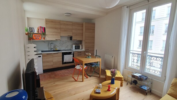 Un espace de vie compact comprenant une cuisine, un coin repas et offrant une vue sur la ville grâce à de grandes fenêtres.