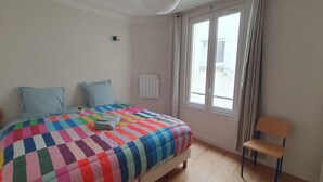 Une chambre à coucher avec un lit, des oreillers, une chaise, un radiateur et une fenêtre.