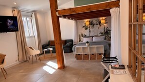 A modern room with a bed, a TV, a desk, and a large window. - Loft with Private Pool, Jacuzzi, AC & Garden – Peaceful Countryside (Saint-Grégoire)