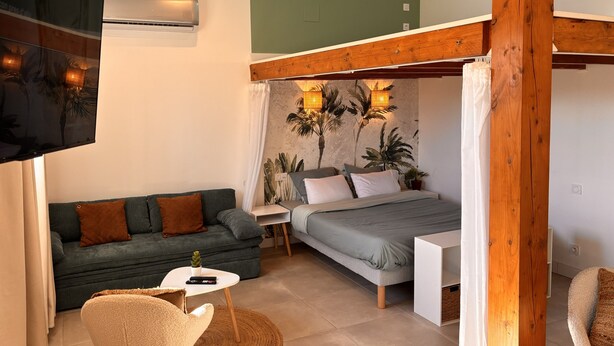 A bedroom with a bed, bedside table, and a small seating area with a chair and table. - Loft with Private Pool, Jacuzzi, AC & Garden – Peaceful Countryside (Saint-Grégoire)