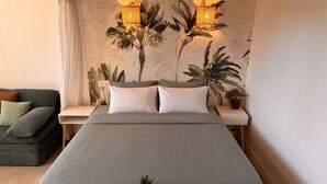 A neatly arranged bedroom with a bed, nightstands, a small table with a plant, and a wall with a palm tree mural. - Loft with Private Pool, Jacuzzi, AC & Garden – Peaceful Countryside (Saint-Grégoire)
