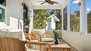 A covered outdoor seating area with wicker furniture, a ceiling fan, and a view of trees and a house. - Cozy home in Sarasota (Sarasota)