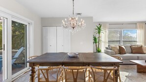 A dining area with a wooden table, chairs, a chandelier, and a view through large windows. - Cozy home in Sarasota (Sarasota)