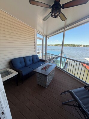 A covered outdoor deck with a blue sofa, a stone coffee table, and a ceiling fan. - Lake Ozark Waterfront Oasis - 4BDR Sleeps 18, Dock, Tiki Bar & High Dive (Lake Ozark)