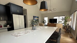 Moderni keittiö, jossa on keskellä sijaitseva saareke, mustat riippuvalaisimet ja kattotuuletin.