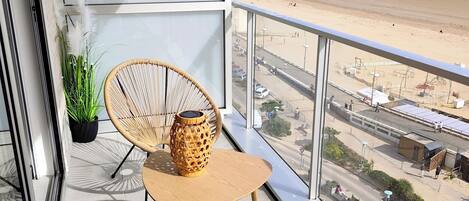 Un balcón con mobiliario de mimbre, una planta en maceta y vista a la playa.