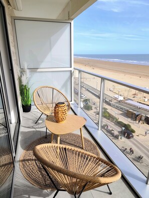 Un balcon agrémenté de meubles en osier, d’une plante en pot et offrant une vue sur la plage.