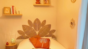 Une chambre à coucher avec un lit, une table de chevet avec une lampe, un mur orné de motifs décoratifs en forme de feuilles, et une étagère avec des livres et un vase.