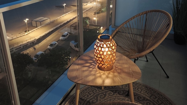 Un balcon agrémenté de chaises en osier, d’une table et d’une lanterne décorative.