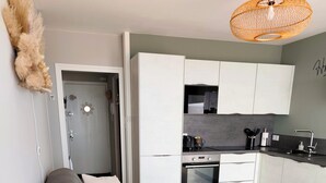 Un espace de vie moderne avec un canapé gris, une petite table à manger en bois, un coin cuisine doté de meubles blancs et un panier en osier.