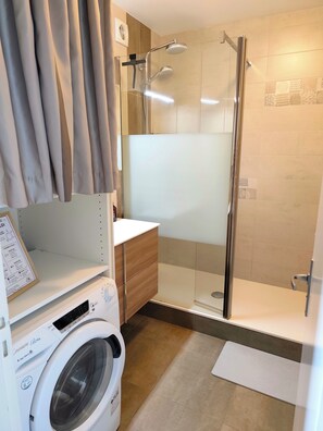 A modern bathroom with a glass shower enclosure, a built-in washing machine, and a vanity with a mirror. - Le 8ème Ciel - Panoramic sea view - Balcony - Wifi (Saint-Jean-de-Monts)
