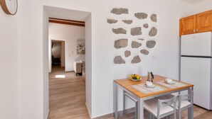 Une cuisine avec un mur en pierre, des placards en bois, un réfrigérateur et une table à manger avec des chaises.