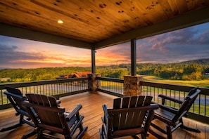 Une terrasse couverte avec des fauteuils Adirondack, une cheminée en pierre et une vue imprenable sur un terrain de golf et une forêt.