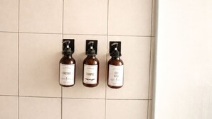 Três frascos de higiene pessoal fixados numa parede com azulejos.
