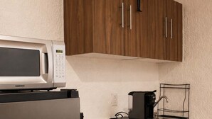 Uma cozinha compacta com micro-ondas, cafeteira e dispensador de água.