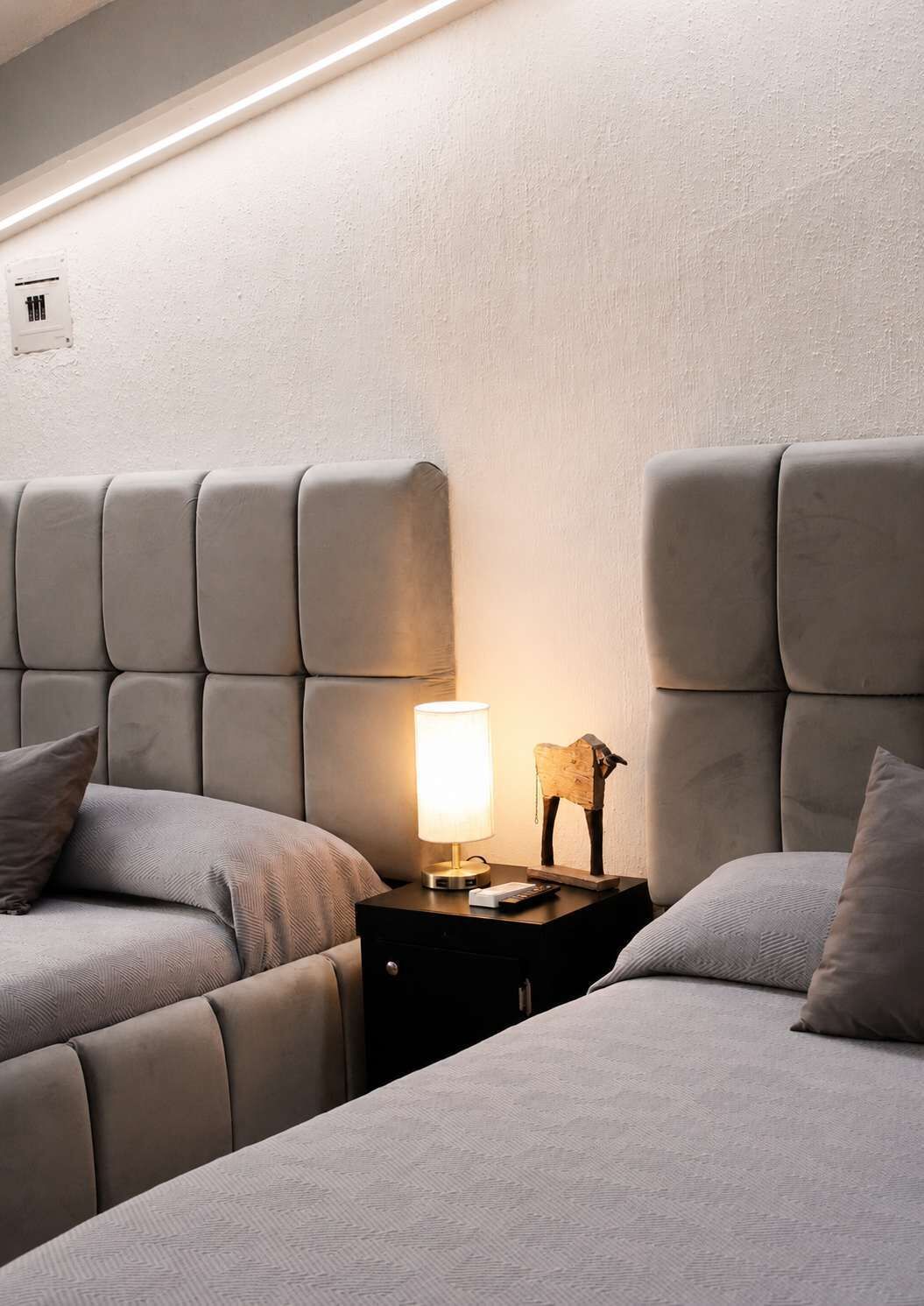 Een hotelkamer met twee bedden, een nachtkastje met een lamp en een wandthermostaat.