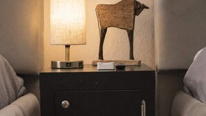 Uma mesinha de cabeceira com uma luminária e uma escultura de vaca de madeira.