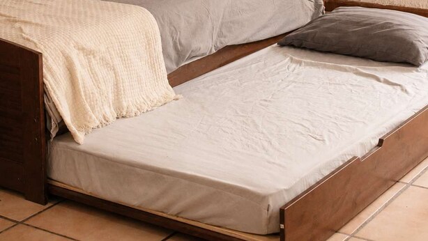 Uma cama de solteiro com estrutura de madeira, um colchão, um travesseiro e um cobertor.