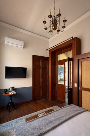 A hotel room with a wooden wardrobe, a television mounted on the wall, a chandelier, and a bed with patterned bedding. - Colonial Luxury in 1830's Hacienda with Balcony (Ciudad de México)