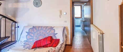 A bedroom with a bed, a clock, a red pillow, a radiator, and a hallway leading to a bathroom.