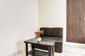 A room with a dark brown sofa, a small table with a white vase of red flowers, and a wooden wardrobe.