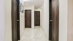 A hallway with marble flooring, dark wooden doors numbered 106, 105, 104, and 102, and a white ceiling with recessed lighting. - Deluxehotel O Nashik Near Vijay Mamta Theatre (Nashik)