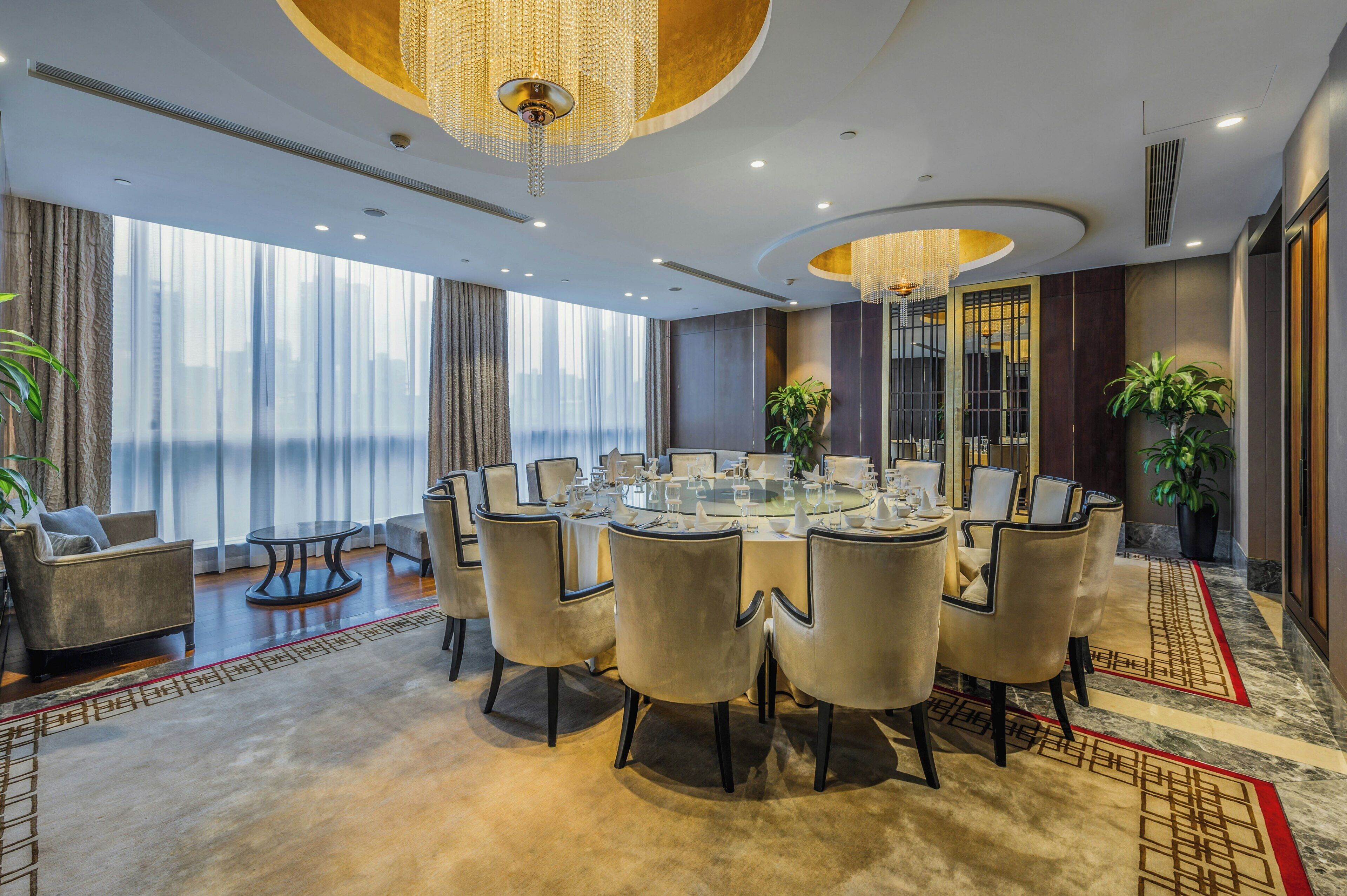 A modern hotel room with a round dining table, comfortable seating, large windows, and decorative lighting.
