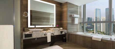 Ein modernes Badezimmer mit einem großen Spiegel, zwei Waschbecken, einer Badewanne und Blick auf eine Stadtlandschaft durch große Fenster.