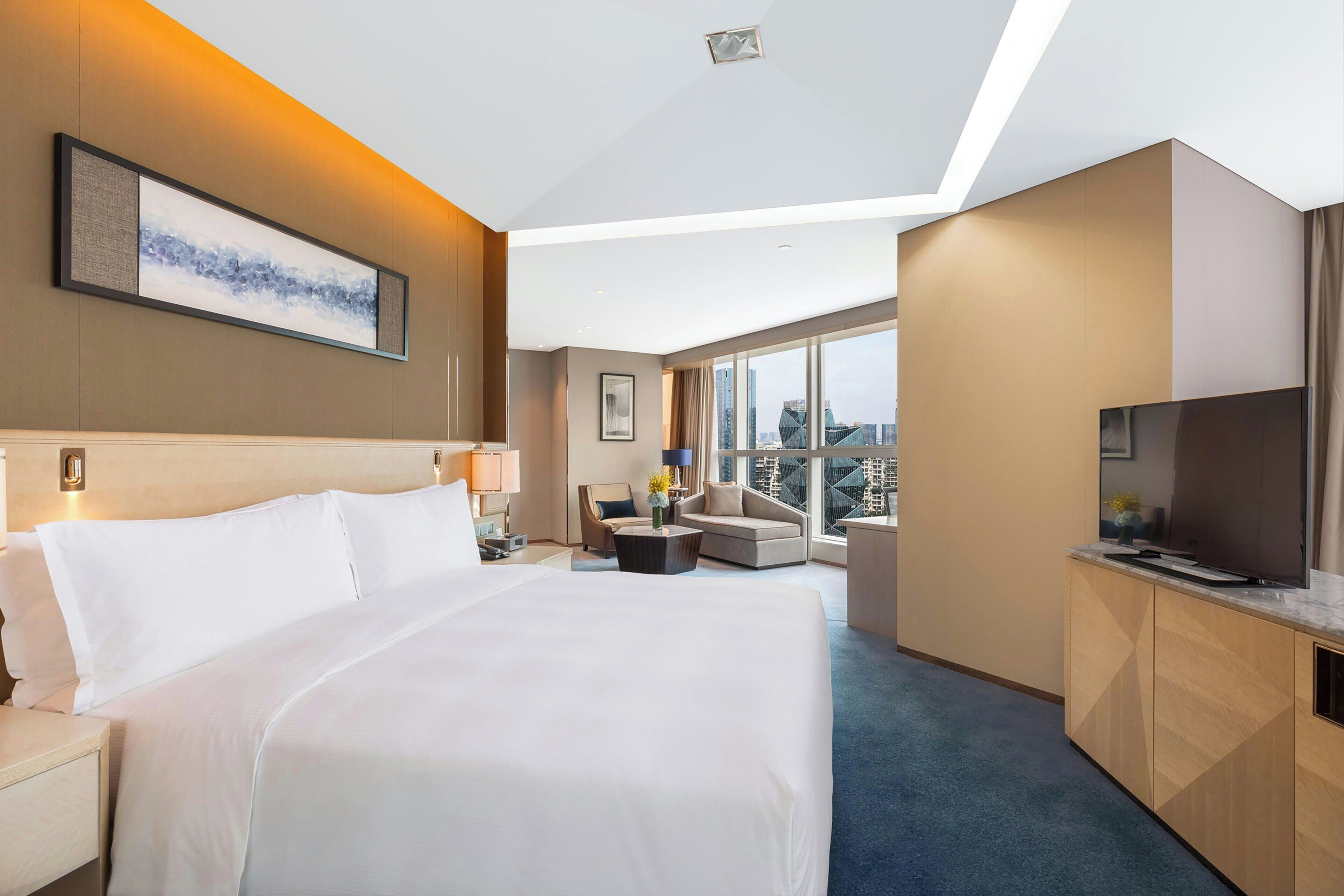 A hotel room with a large bed, a sofa, a TV, and a city view.