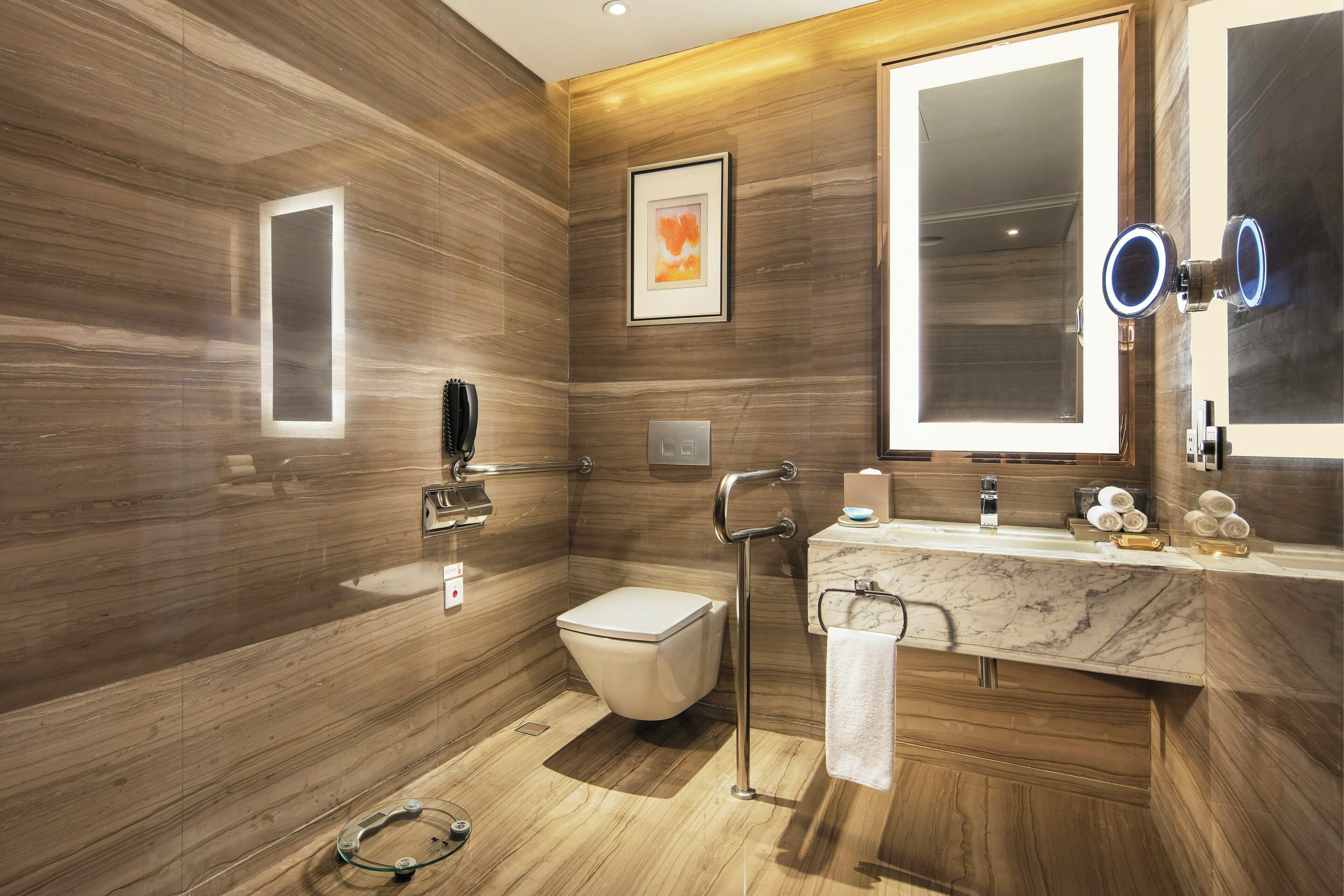 Une salle de bain moderne avec un lavabo en marbre, des toilettes, un miroir avec un éclairage intégré et un tableau encadré accroché au mur.