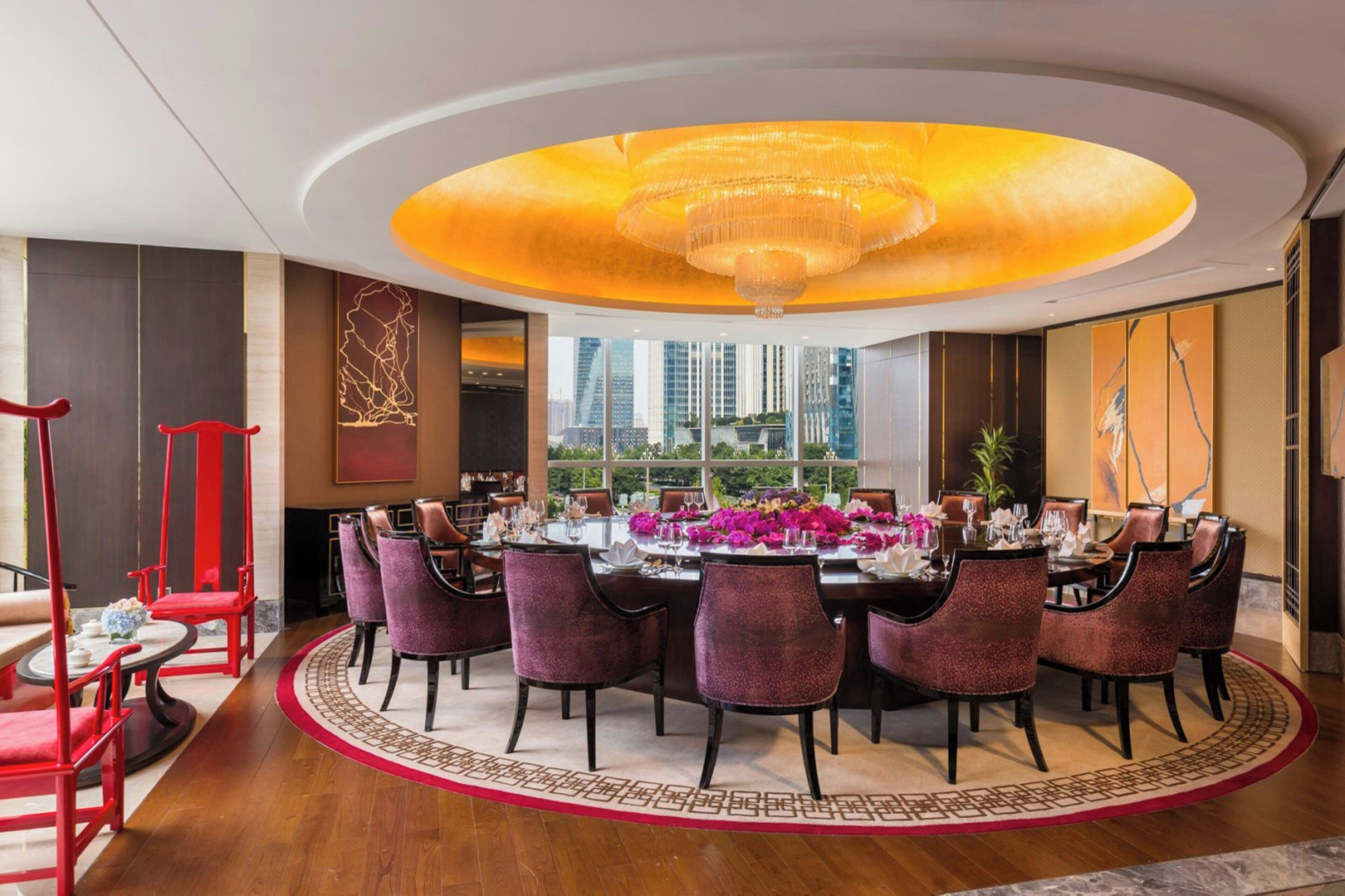 A dining area with a round table, red chairs, and a chandelier.