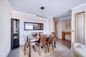 A dining area with a wooden table, chairs, a chandelier, a bookshelf, and a mirror on the wall. - Angamos Coast Luminous Apartment 3D in Reñaca (Viña del Mar)