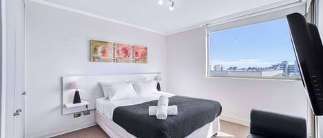 Habitación de hotel moderna con una cama grande, un sillón de cuero negro, vistas a la ciudad y obras de arte en la pared.